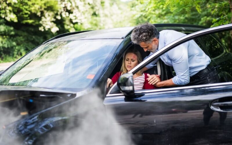 Man assisting an injured woman out of a car after an accident.